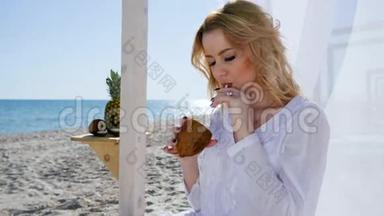 美丽的女人坐在平房里，岸上有白色的窗帘，女孩躺在海滩上，喝着<strong>椰子汁</strong>，